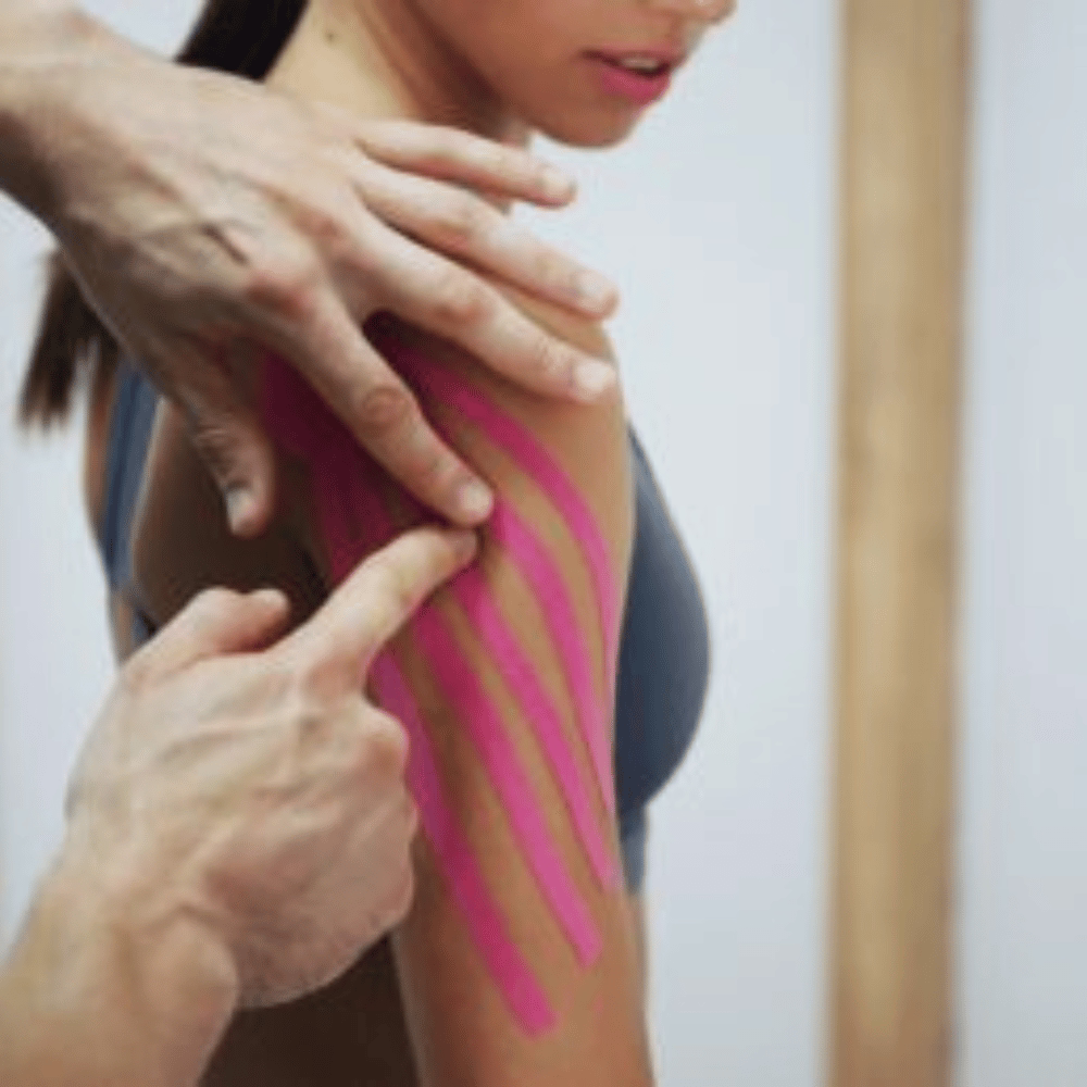 Therapeut bringt Kinesis Tape an Schulter einer jungen Frau an