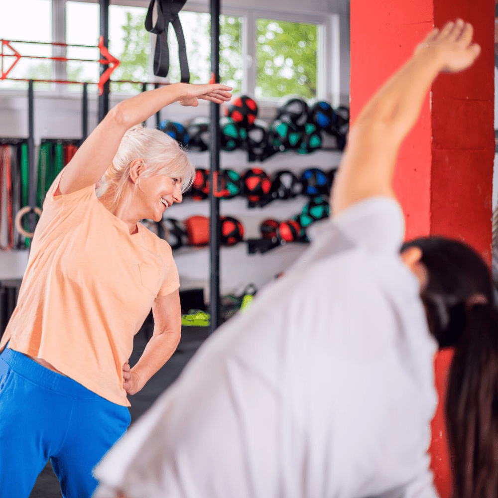 Ältere Frau macht unter Anleitung Dehnübung im Rehasportbereich